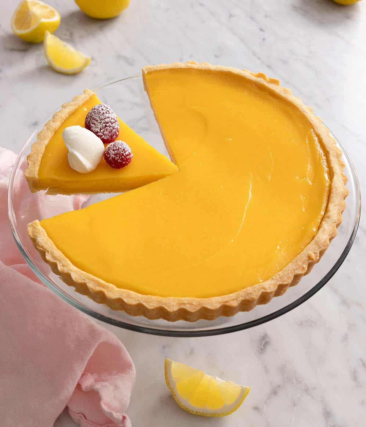 A lemon tart on a cake stand with a slice cut.
