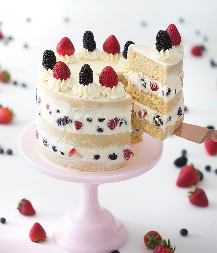 picture of a three layer berry cake on a pink cake stand with a piece being removed