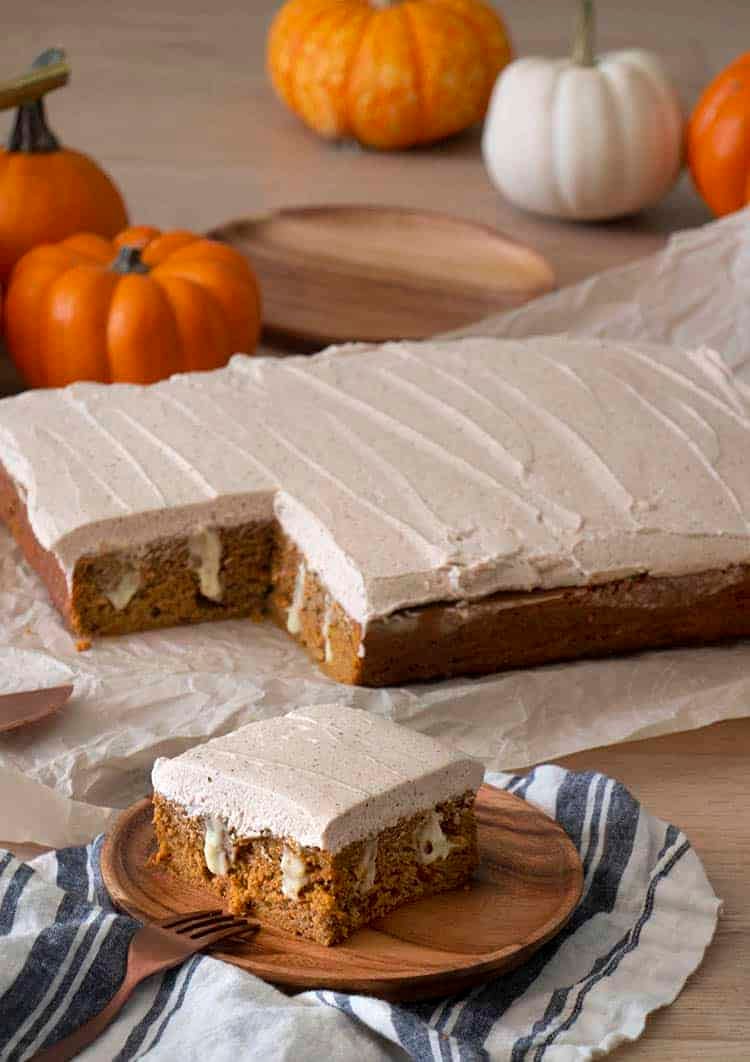 A pumpkin poke cake covered in brown butter frosting with a pice in the foreground.