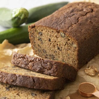 A loaf of sliced zucchini bread next to some fresh zucchinis.