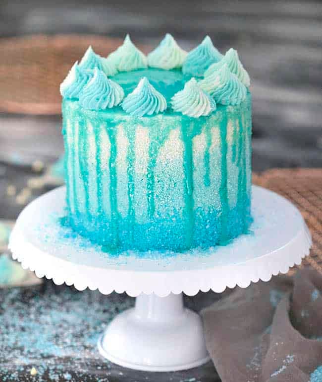 A winter wonderland cake covered in blue sparkles with a blue drip.