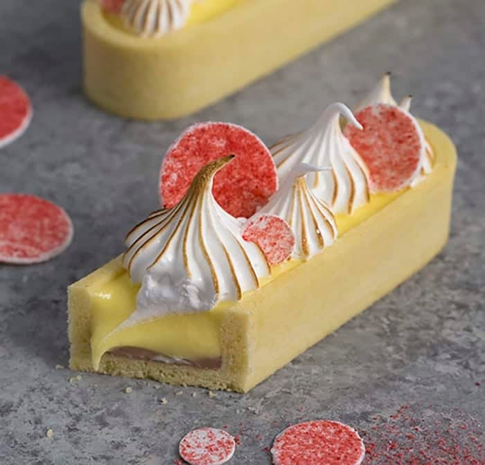 A close up image of a lemon curd tart with pink circles on top and toasted meringue dollops.