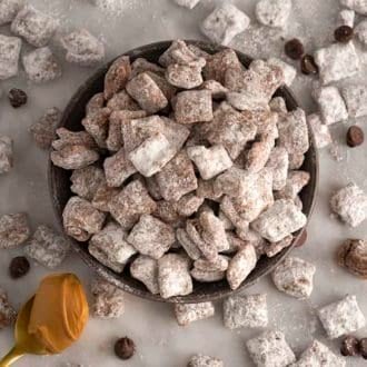 A bowl of puppy chow with chocolate chips scattered around on a marble table.