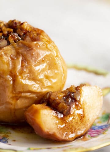 A close up of a baked apple sitting on a plate with a slice beside it.