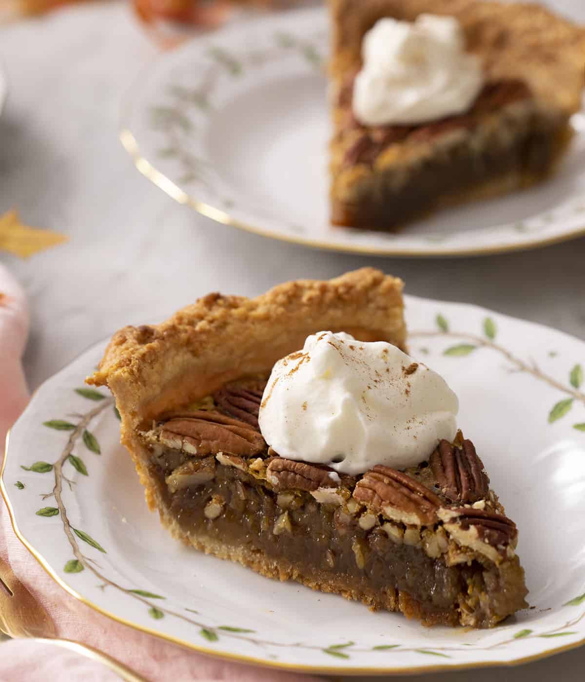 A piece of pecan pie on a plate with another in the background.