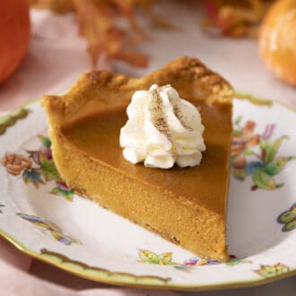 A piece of pumpkin pie with whipped cream on a plate.