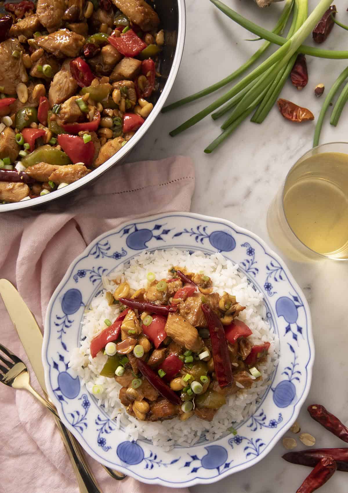 An overhead shot of Kung Pao chicken on a blue plate with a glass of wine beside it