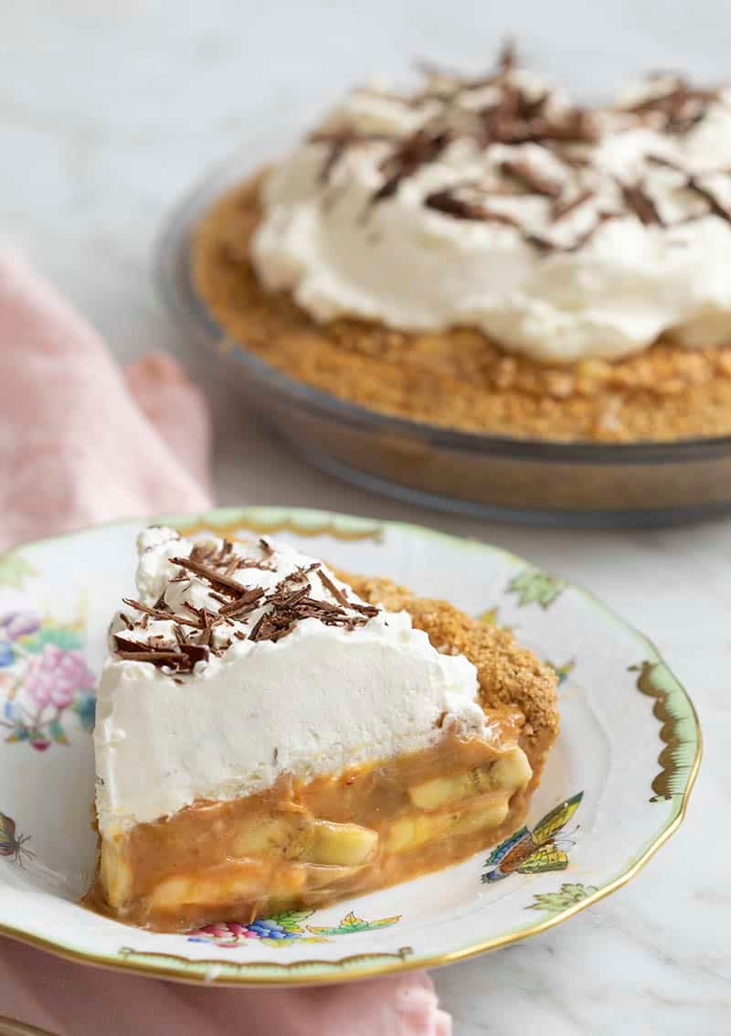 A piece of delicious banoffee pie in the foreground with the whole pie behind it.