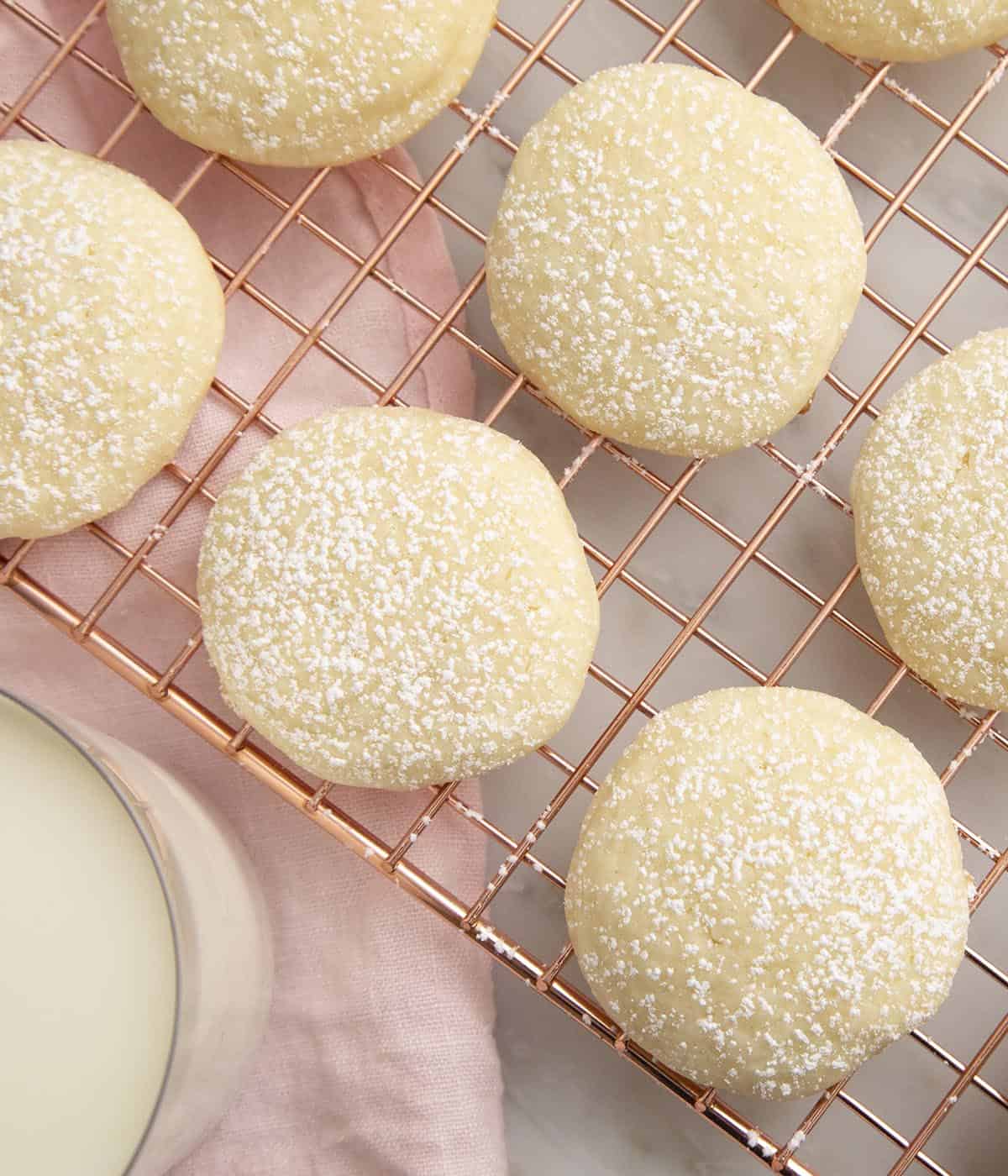 cream cheese cookies dusted with powdered sugar on a copper cooling rack.