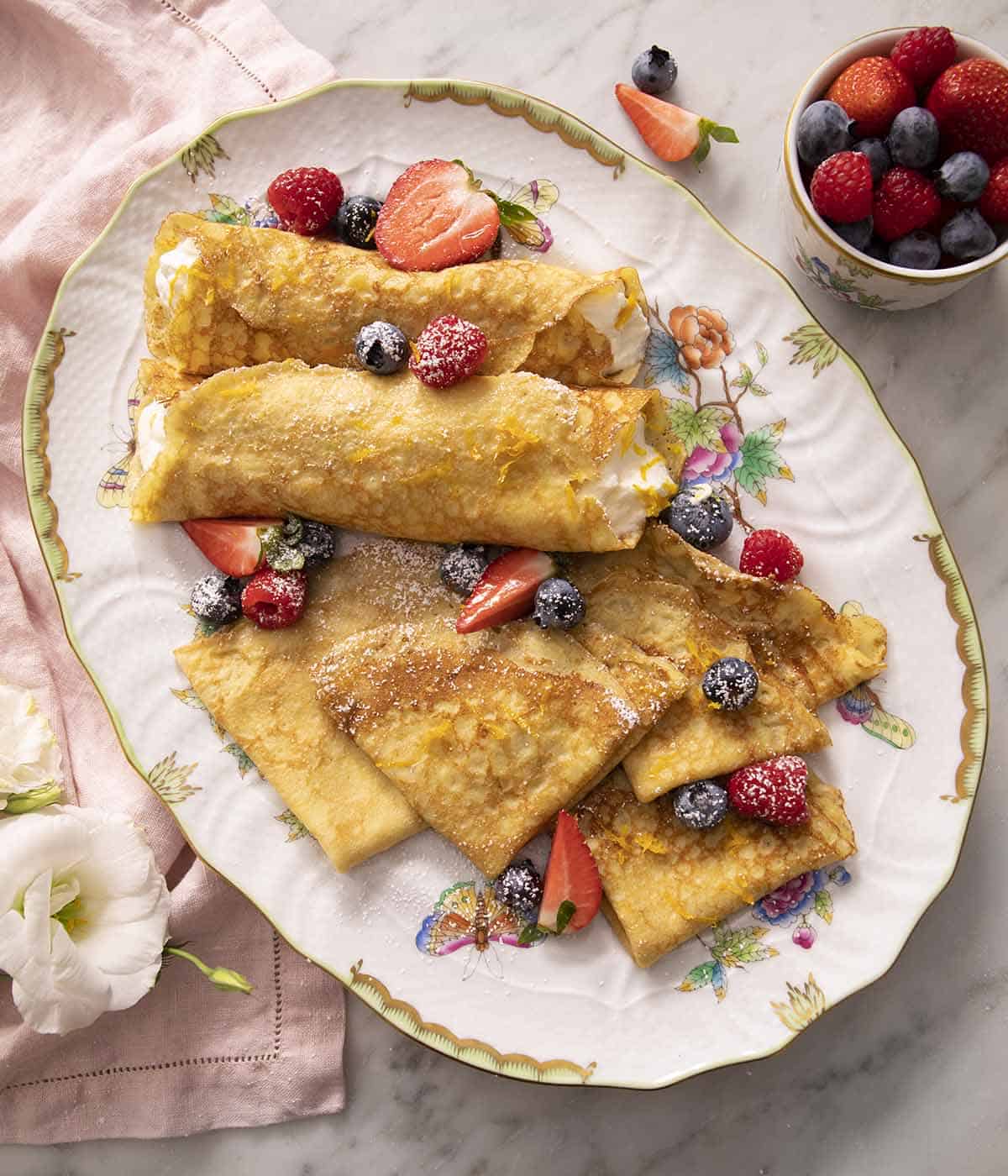 A large platter with crepes and berries on a marble surface.