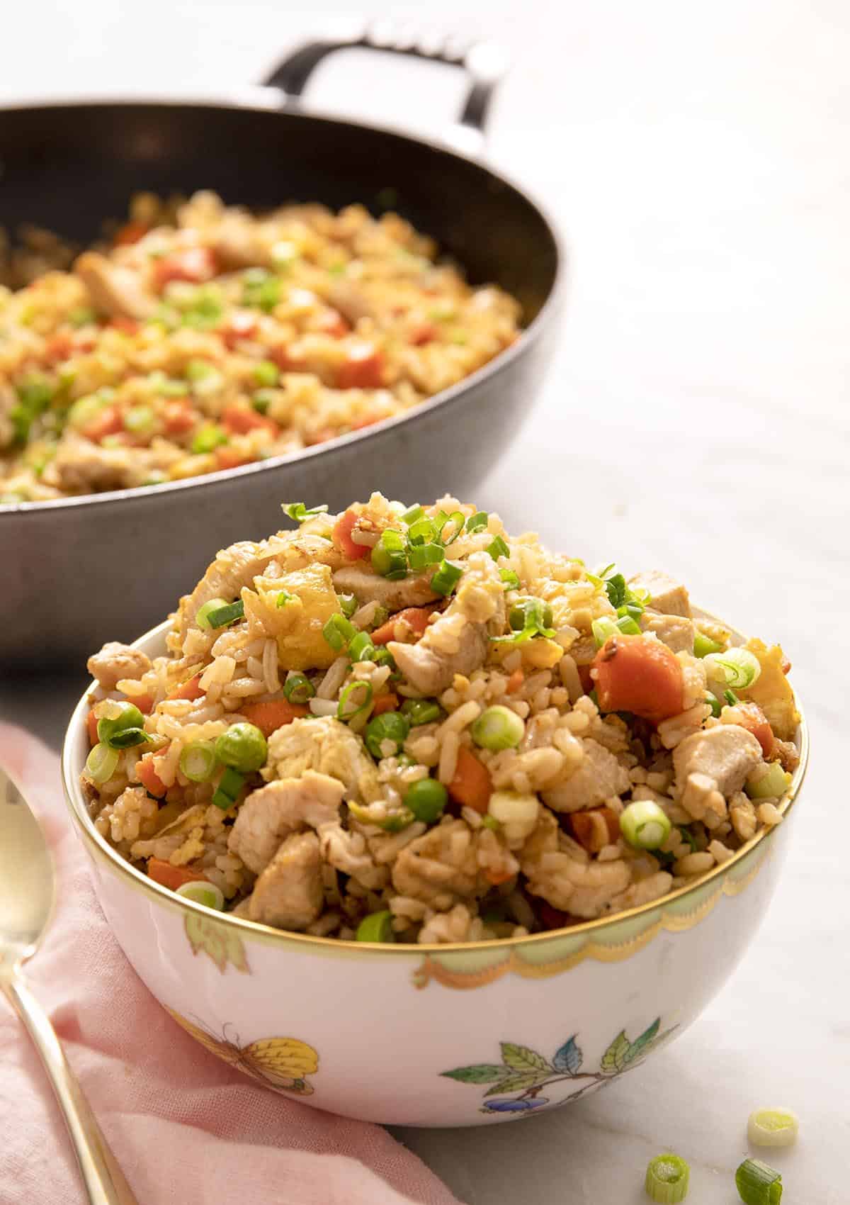 Chicken fried rice in a white bowl with a skillet behind it
