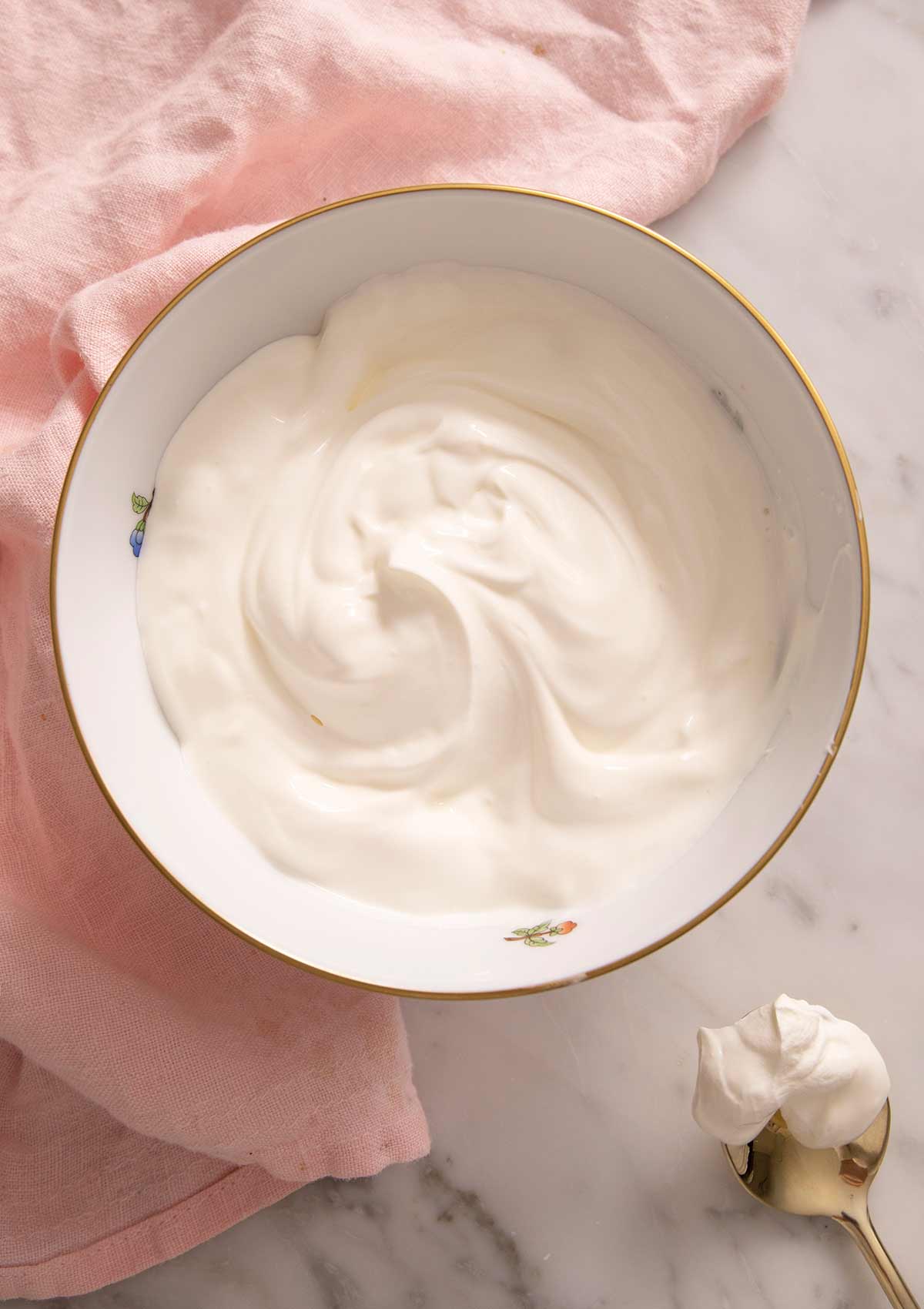 Sour cream in a bowl with a gold spoon beside it.