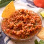 A close up of a bowl of salsa with a chip dunked into it.
