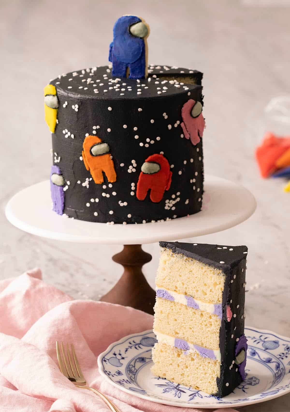 A slice of among us cake on a plate with the whole cake in the background