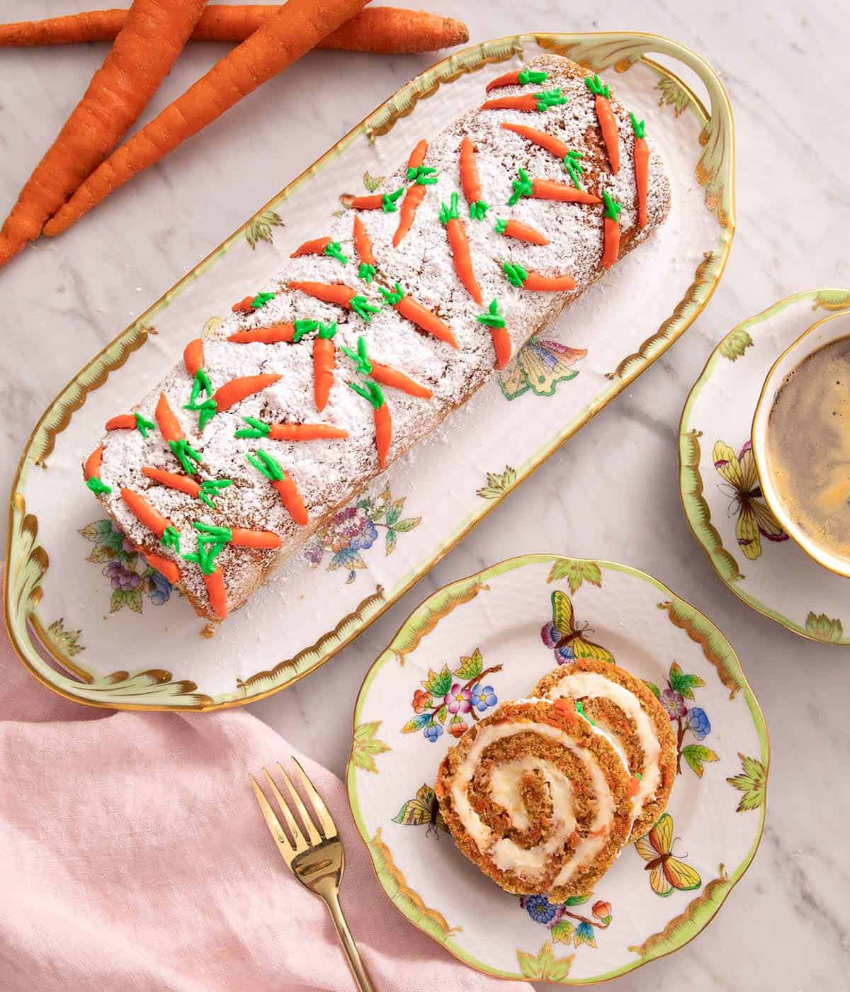 An overhead shot of a carrot cake roll on a serving plate and two slices cut
