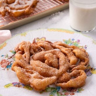 Pinterest graphic of a funnel cake on a plate with more in the background on a cooling rack.