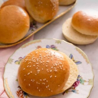 Pinterest graphic of a plate of brioche bun with sesame seeds on top with a platter of brioche buns in the background.