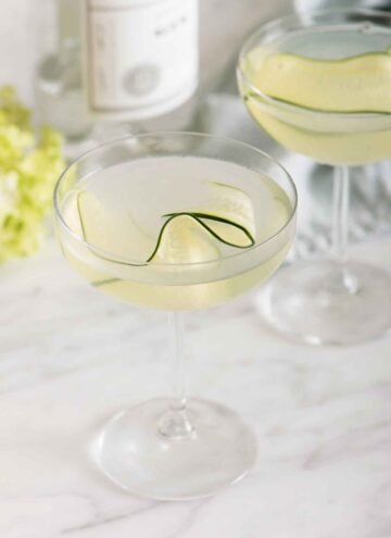 Two glasses of cucumber martini with one in front of the other. Both has a thin slice of cucumber as garnish.