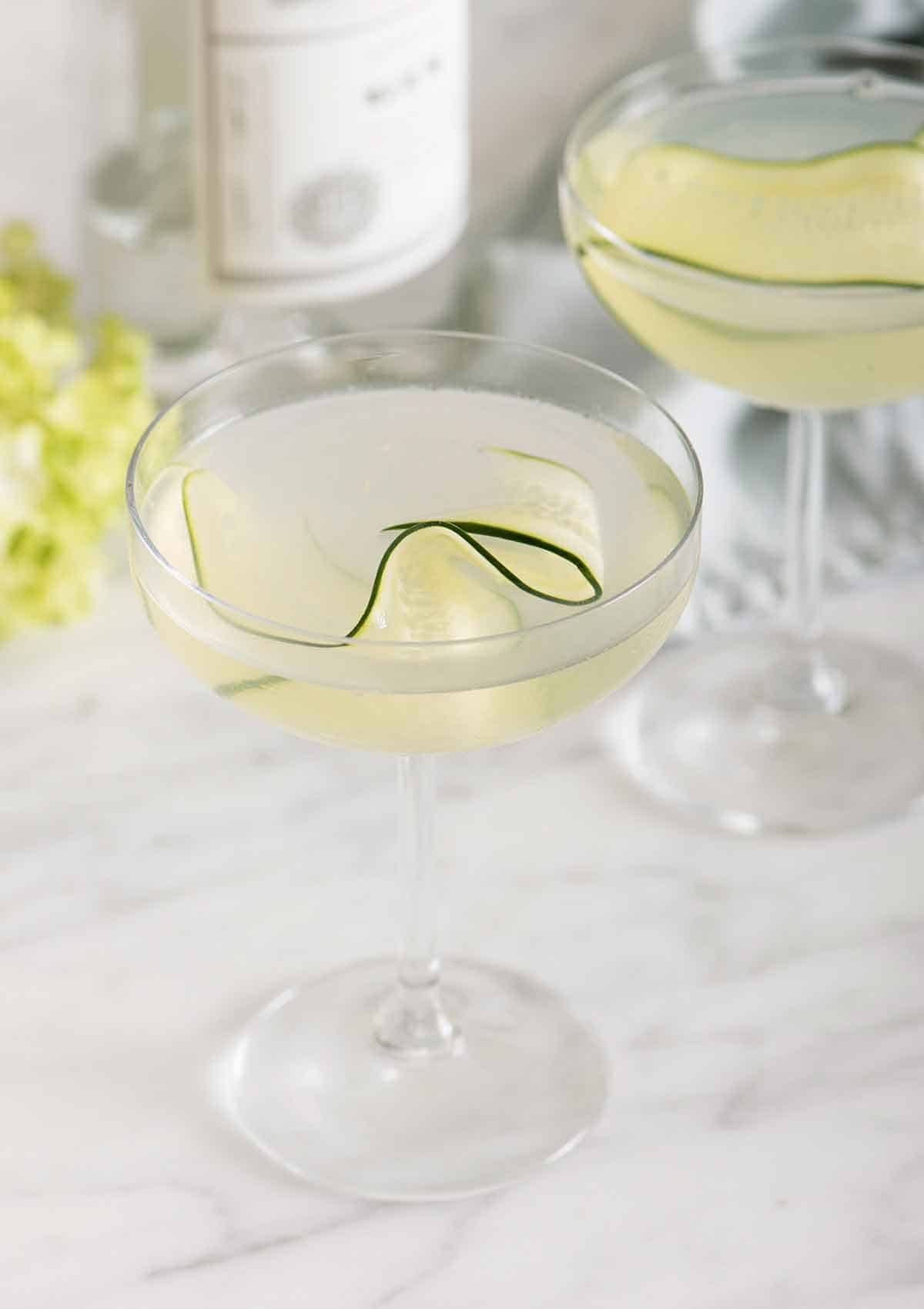 Two glasses of cucumber martini with one in front of the other. Both has a thin slice of cucumber as garnish.