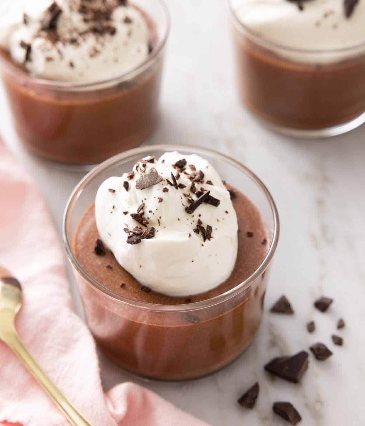 One of three chocolate mousse in focus with a dollop of whipped cream and chocolate bits on top.