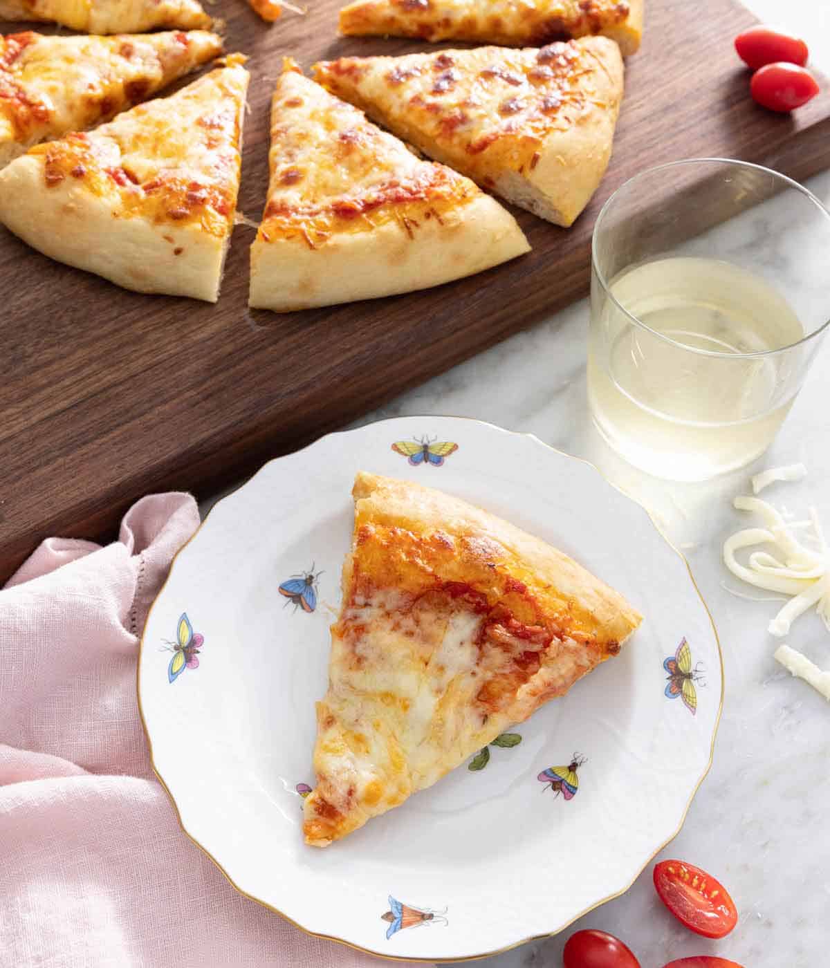 A plate with a slice of cheese pizza in front of a glass and more pizza.