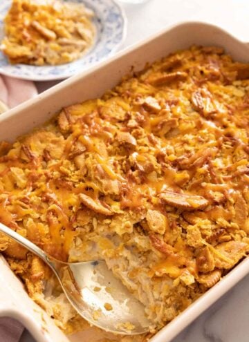 A chicken casserole with a serving removed and a spoon inside the baking dish.