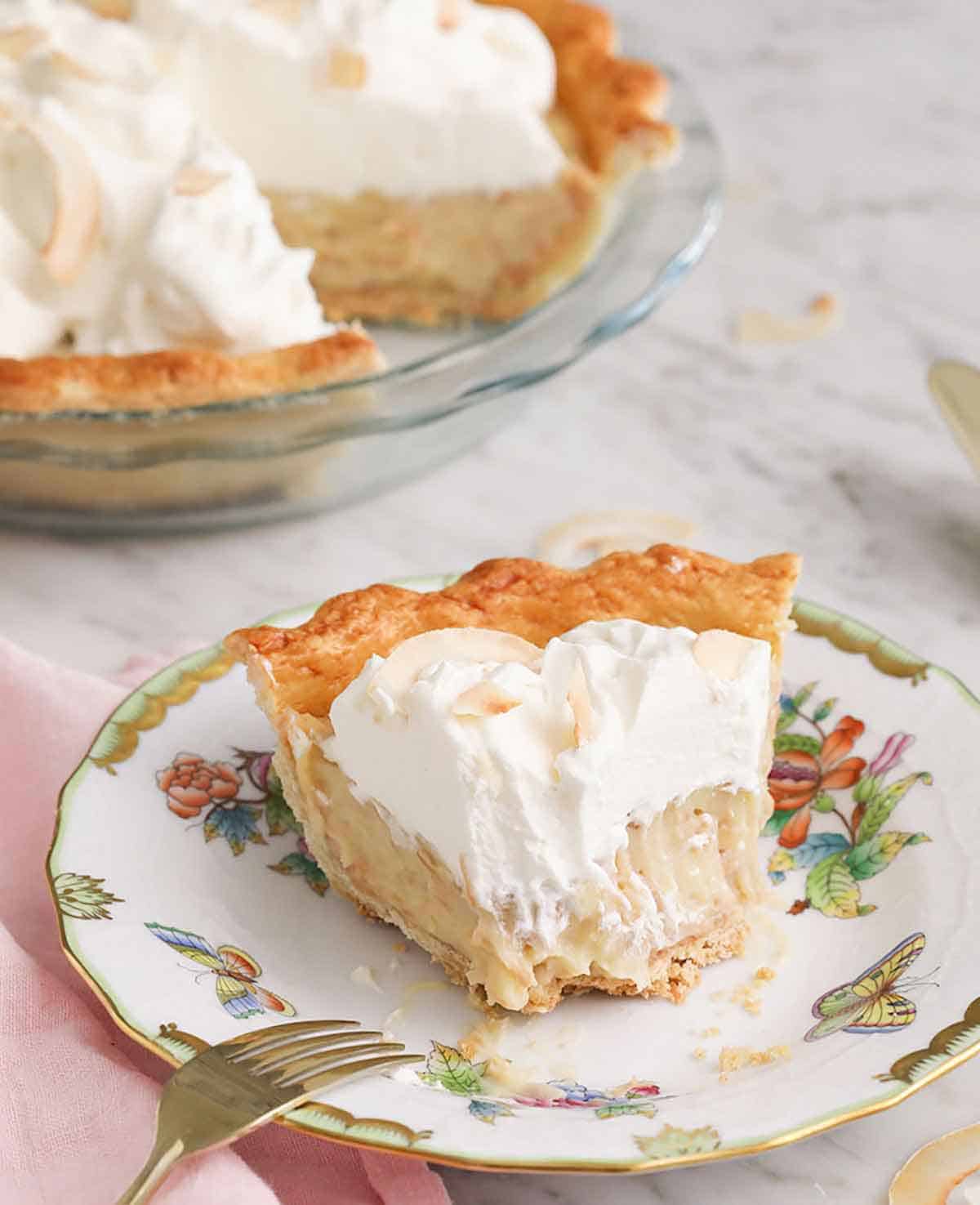 A plate with a slice of coconut cream pie with a bite taken out.