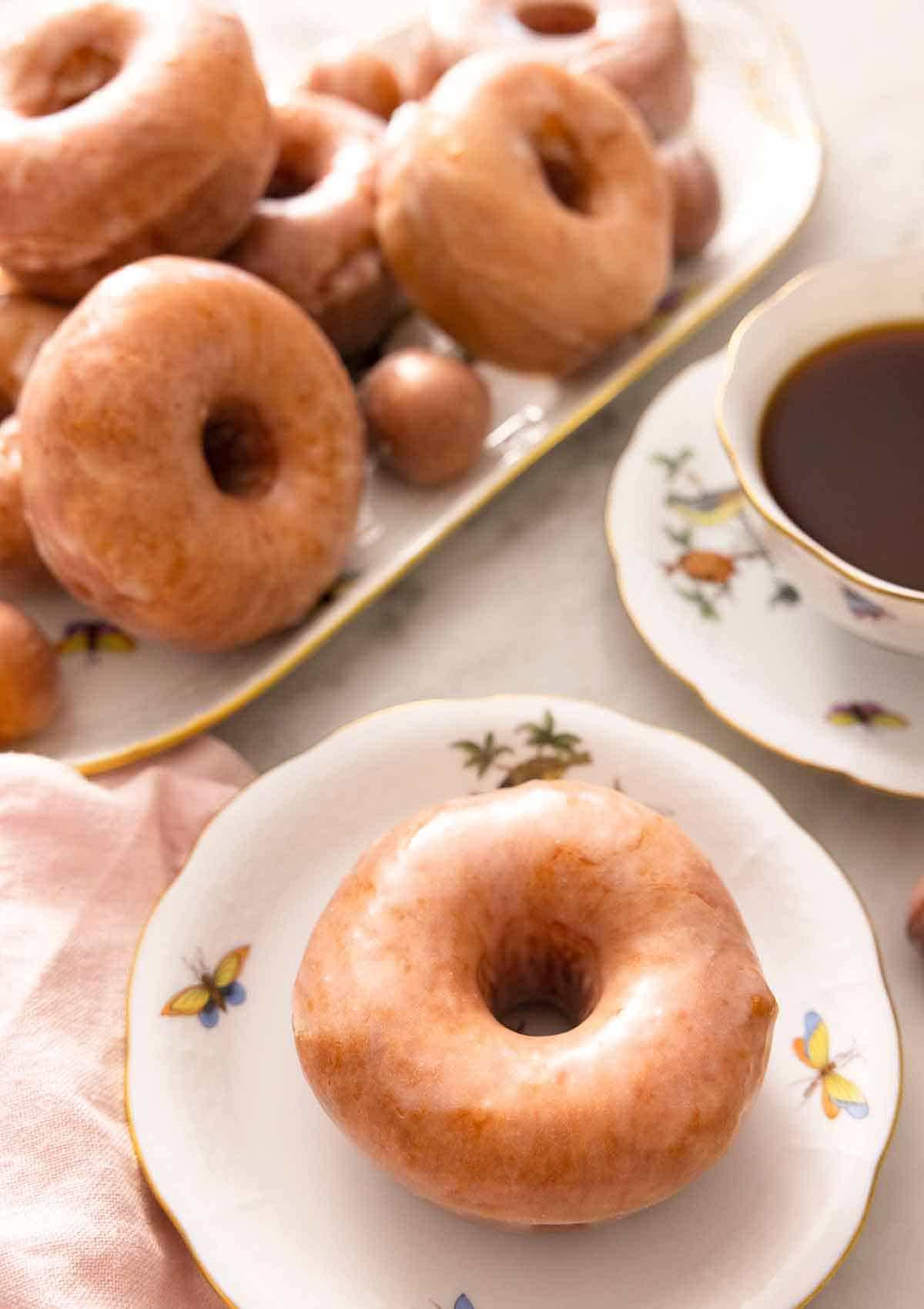 A plate with a glazed donut with a platter with more behind it.