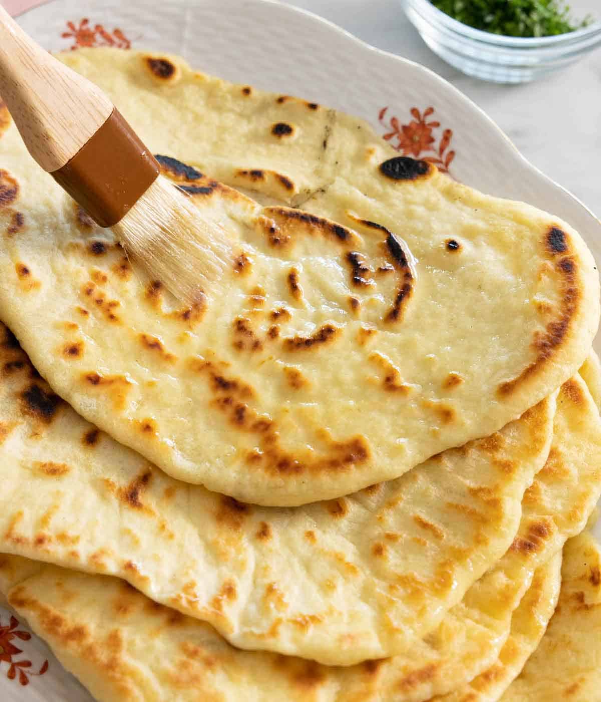 Butter brushed onto a stack of naan bread.