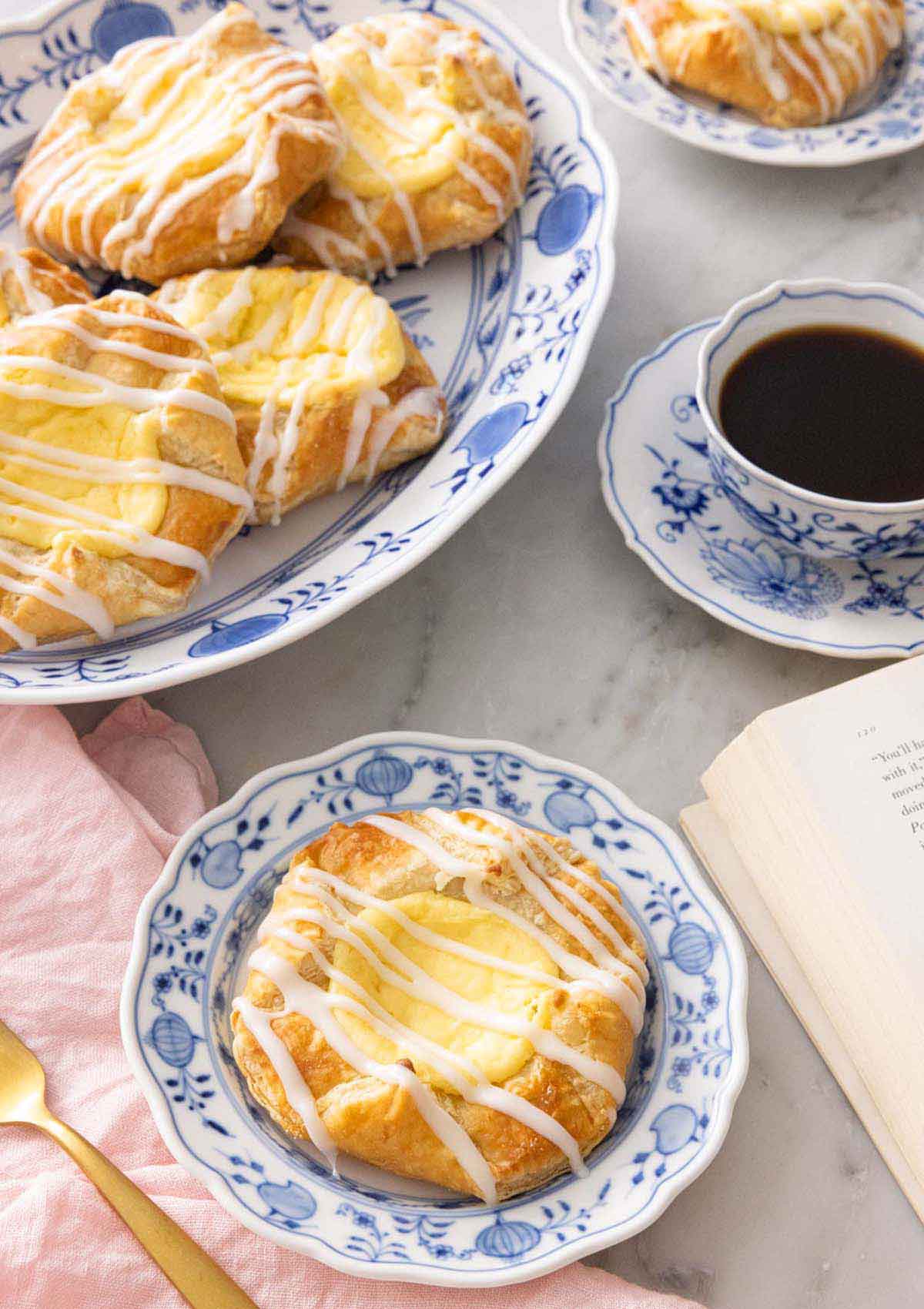 A plate with cheese danish in front of a platter with more.