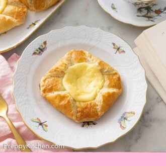 A plate with a cheese danish in front of a cup of tea.