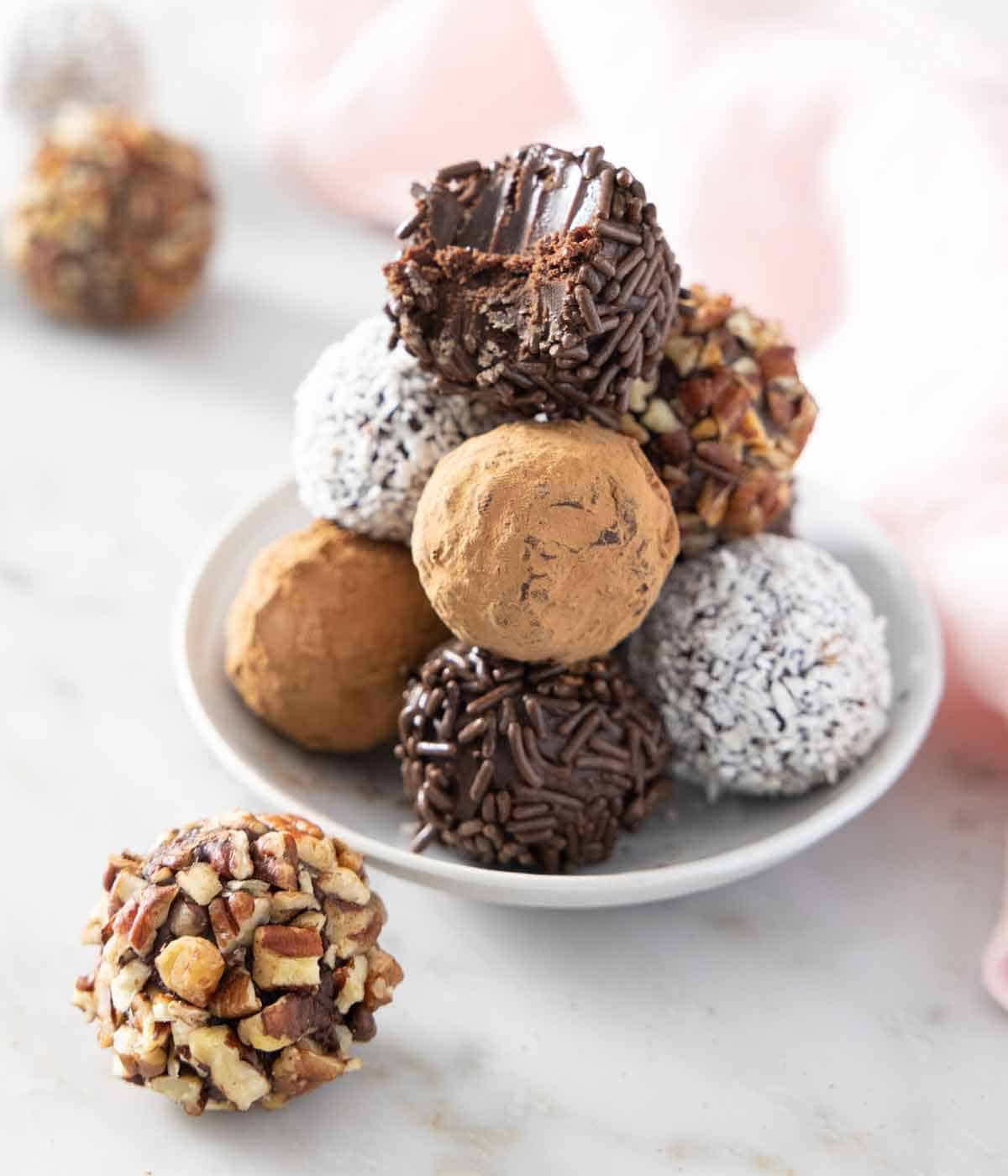 A plate with a stack of classic chocolate truffles and one in front.
