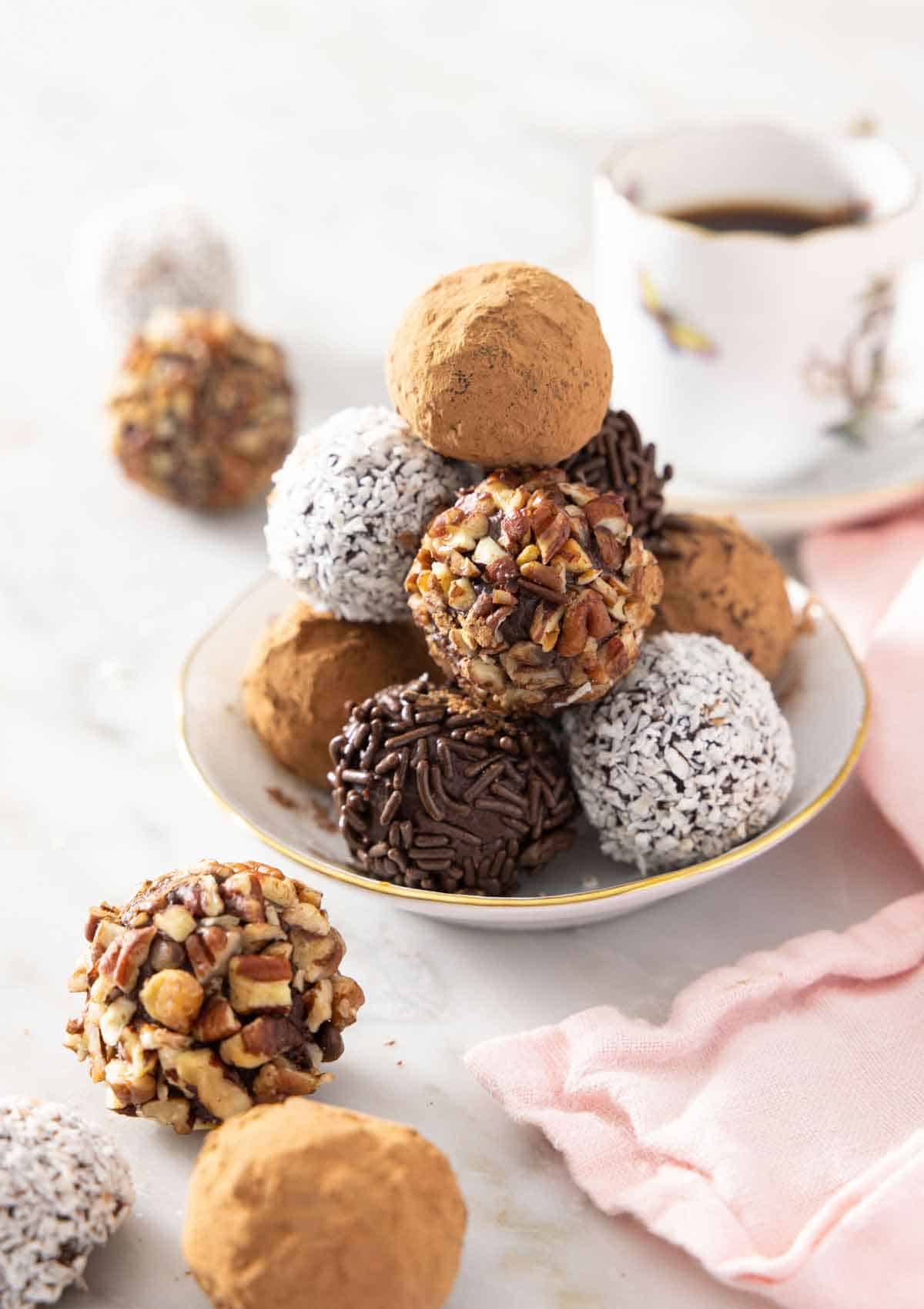 A plate with a pile of chocolate truffles with different coatings. A few in front.