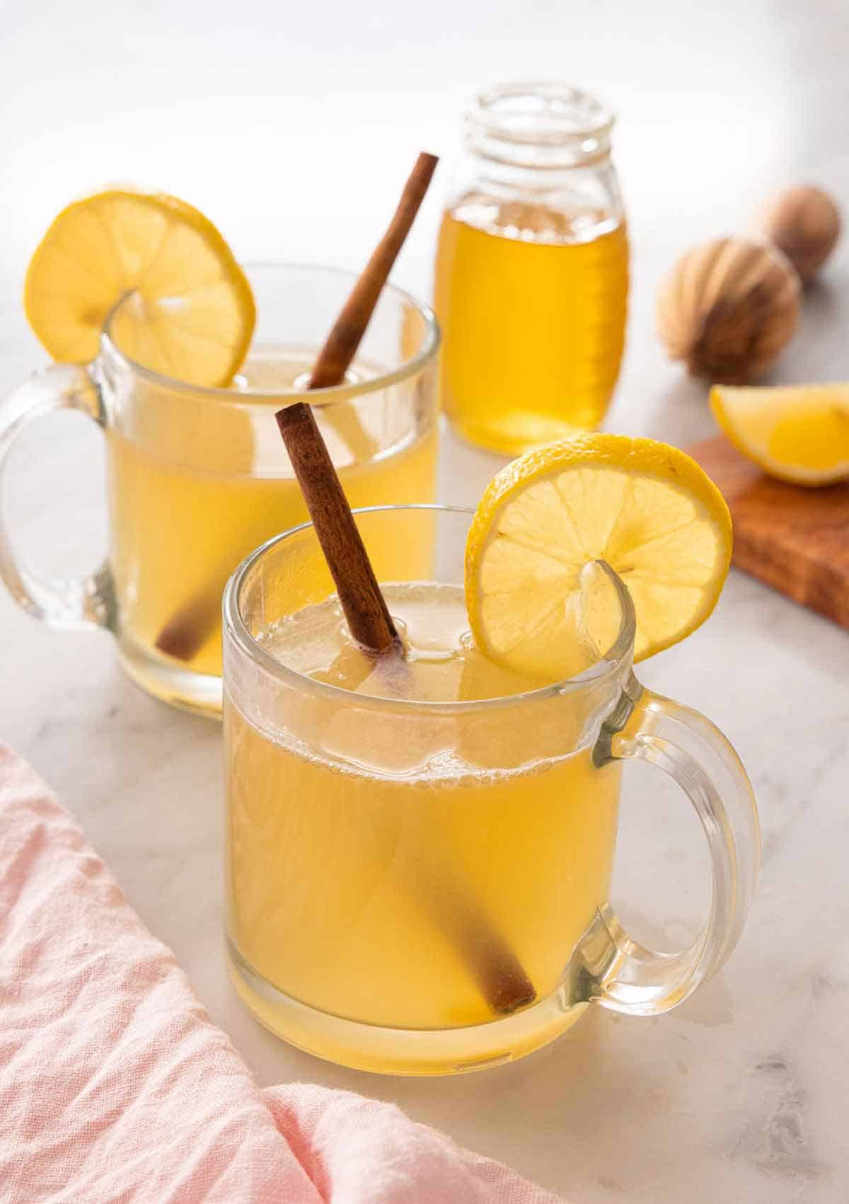A glass of hot toddy in front of a second on and a jar of honey.