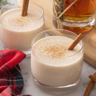 Two glasses of coquito with a bottle of rum in the background with a red linen in front.