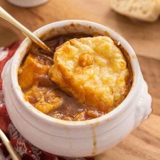A bowl of French onion soup with a spoon inserted and some dripping over the bowl.