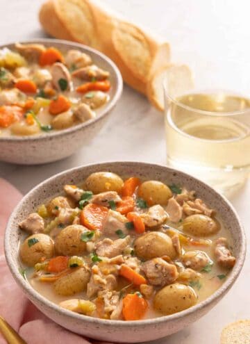 Two bowls of chicken stew, one in front, both garnished with fresh herbs.