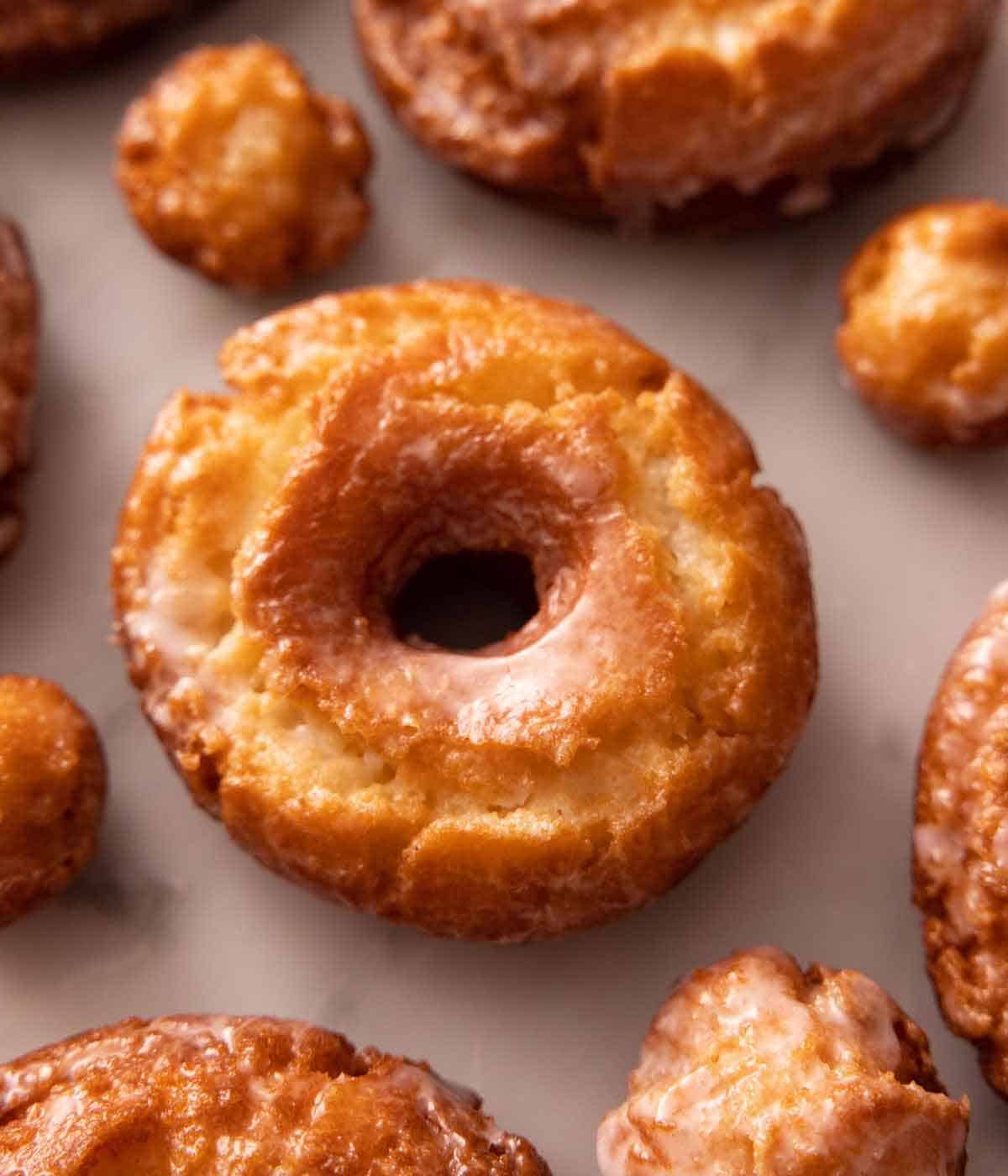 An old fashioned donut surrounded by donut holes and additional donuts.