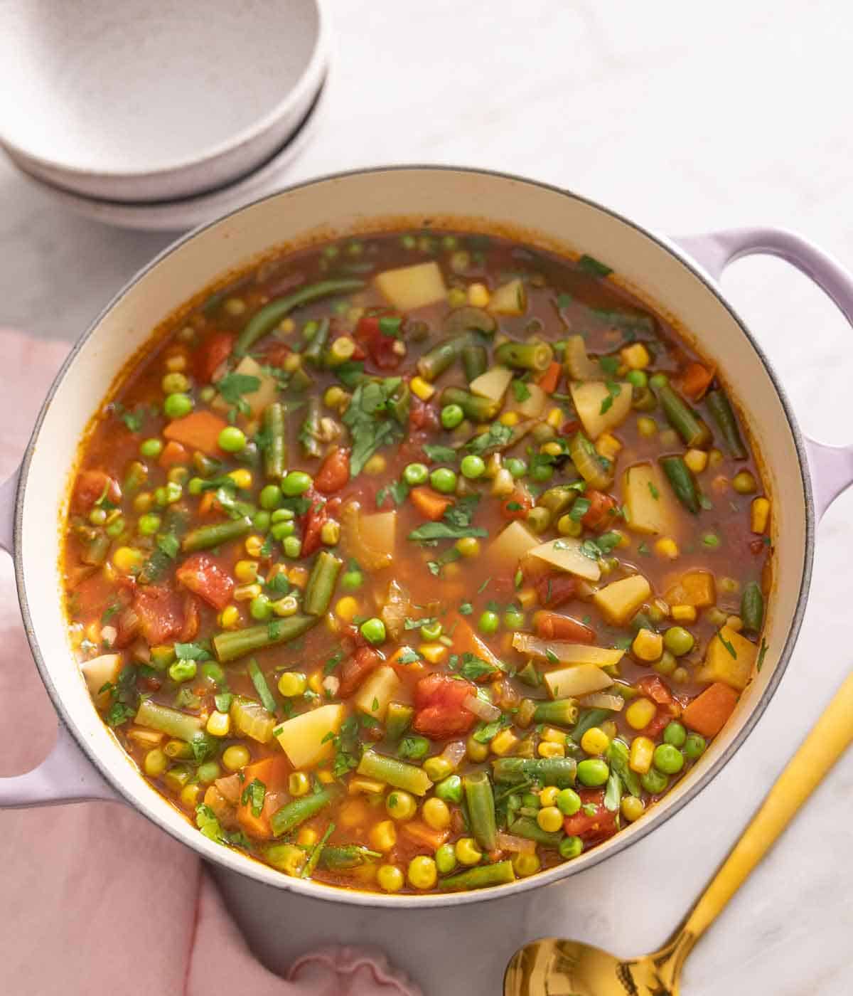 A purple dutch oven with vegetable soup.