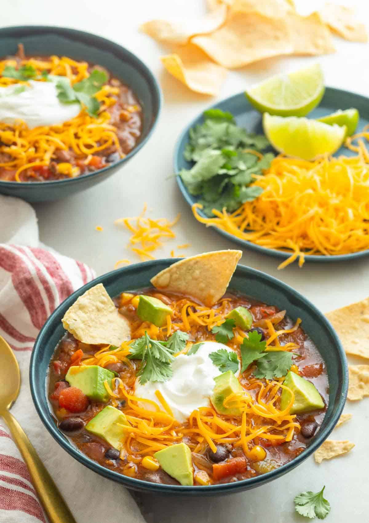 Two bowls of taco soup with a plate of toppings on the side.