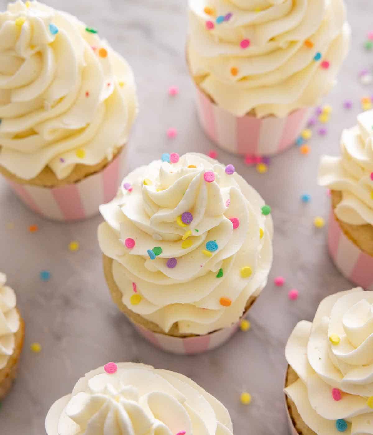 Angled view of multiple Italian buttercream topped cupcakes with sprinkles on top.