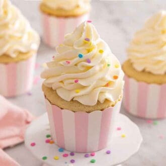 A cupcake on a mini stand with Italian buttercream piped on top. More cupcakes in the background.