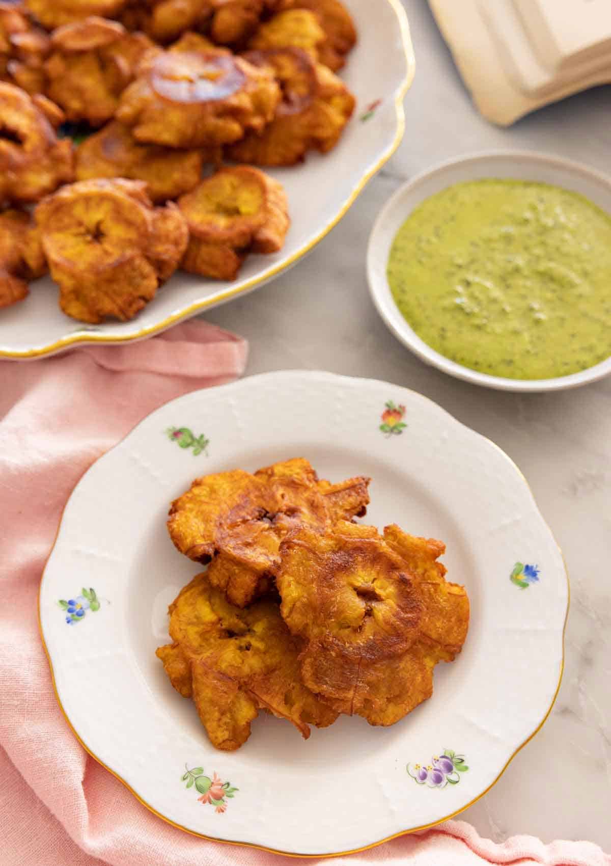 A plate with tostones with additional on a platter in the back along with dip.