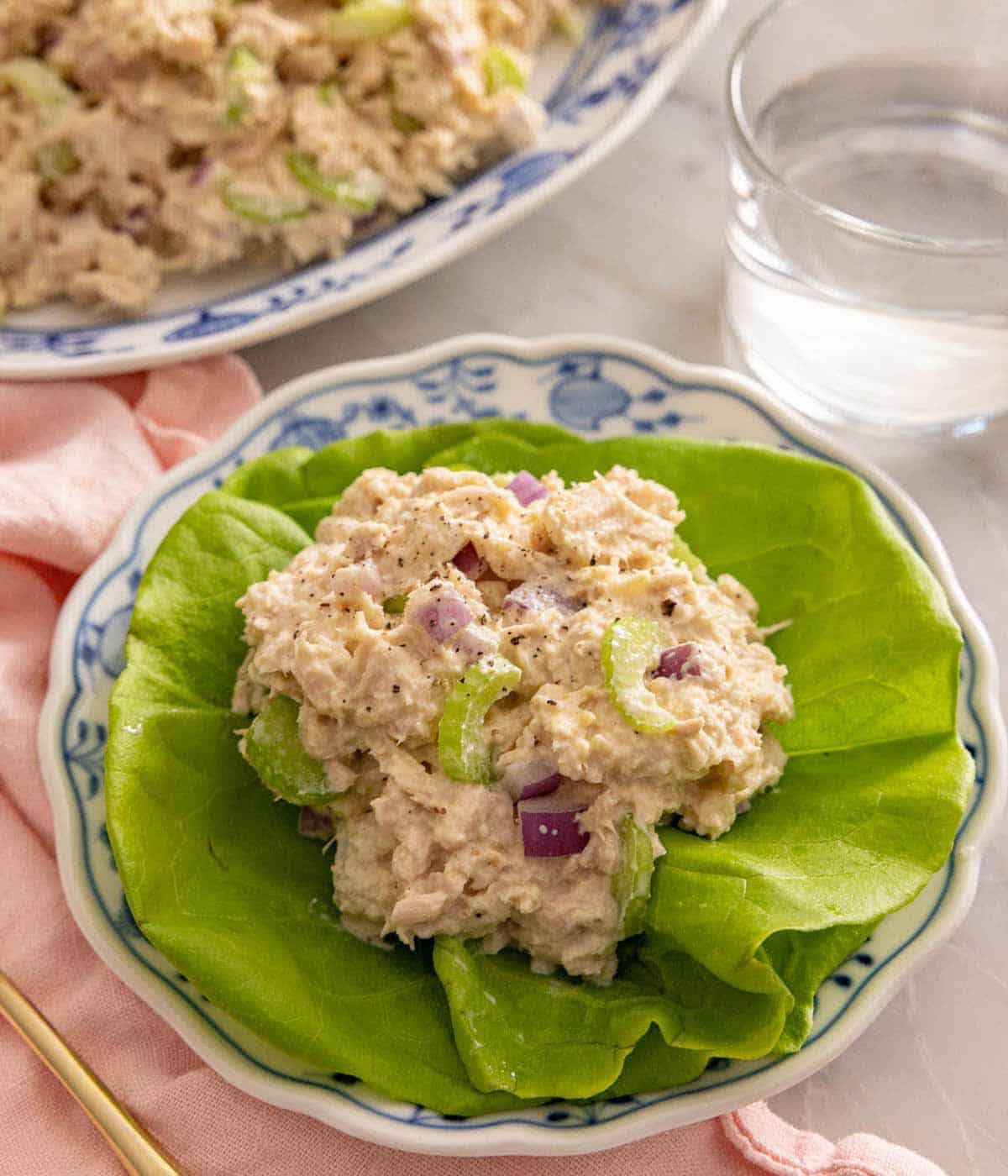 A plate with tuna salad on lettuce by a glass of water.