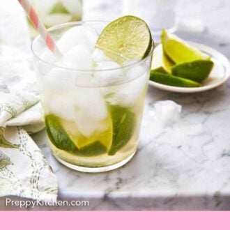 Pinterest graphic of a glass of caipirinha with a fresh slice of lime on top of the ice with more limes in the background.