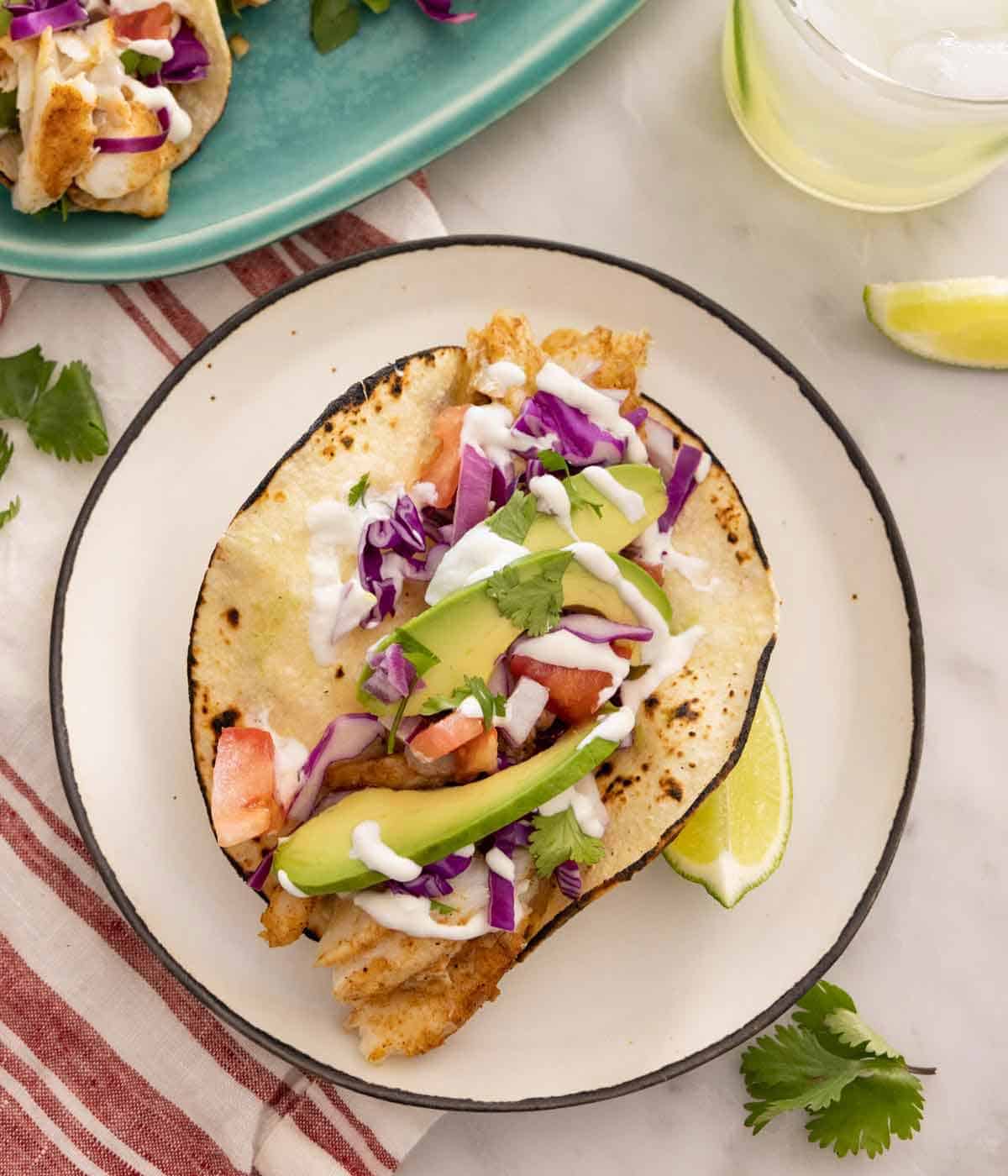 Overhead view of a fish taco on a plate along with a lime wedge beside it.