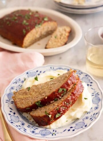 Two slices of turkey meatloaf on top of mashed potatoes with the rest of the meatloaf in the background.