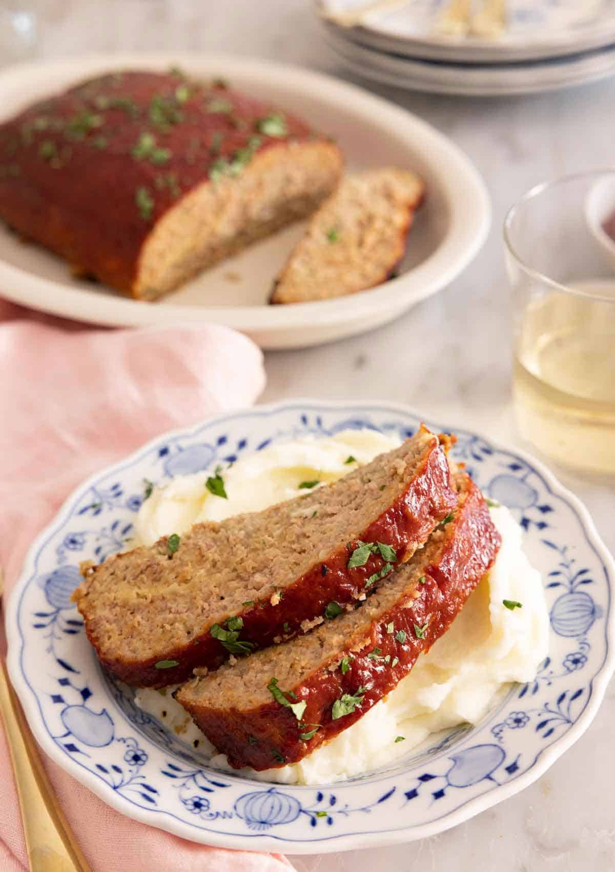 Two slices of turkey meatloaf on top of mashed potatoes with the rest of the meatloaf in the background.
