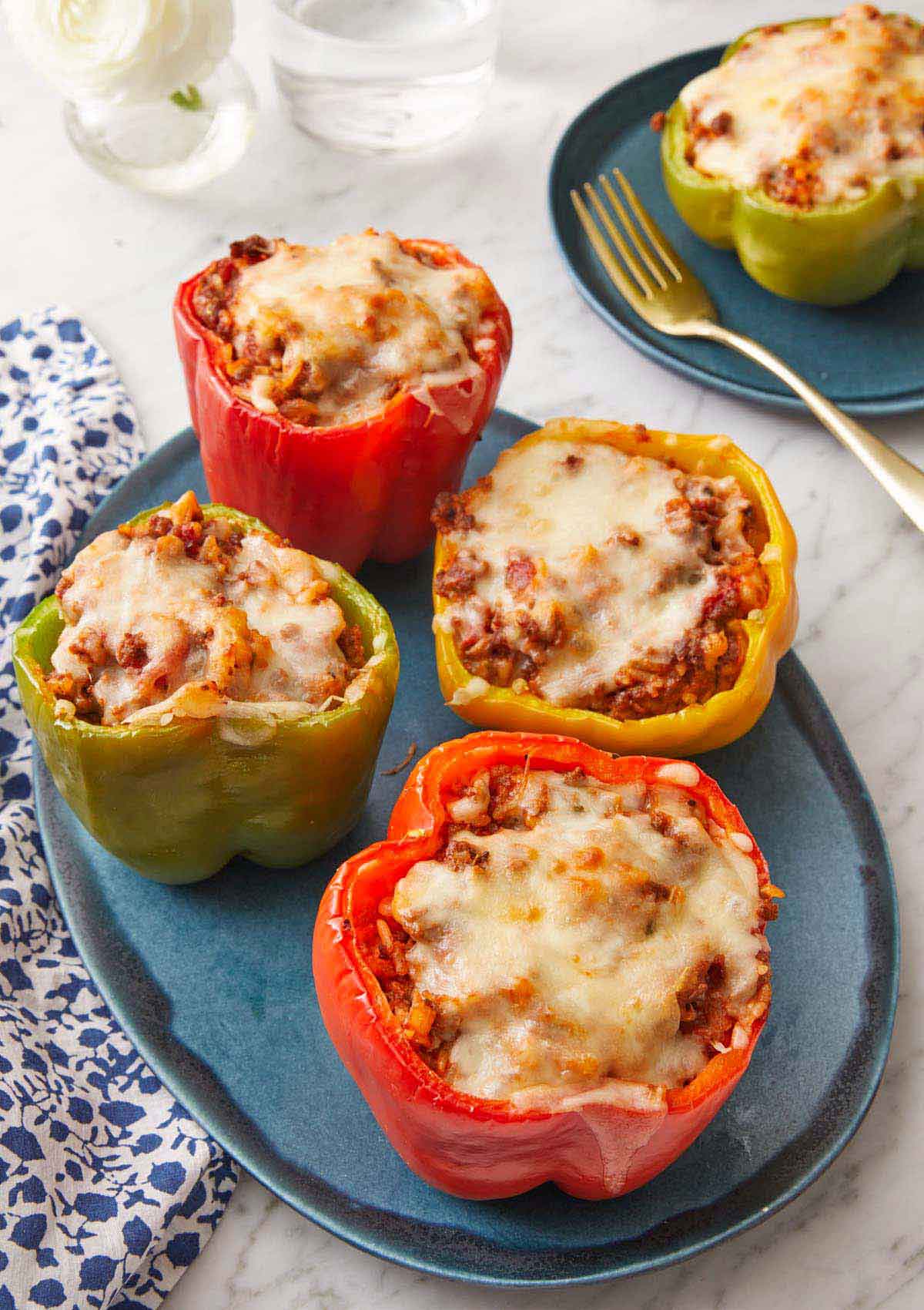 A platter with four stuffed peppers with a plate with a single one in the background.