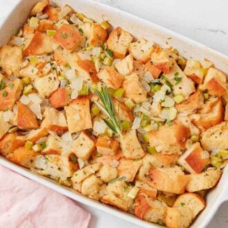 Overhead view of a white baking dish filled with stuffing with a piece of fresh rosemary on top.